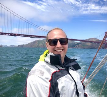 Torben Yjord-Jackson is pictured sailing. He is wearing a white jacket and the Golden Gate Bridge is pictured in the background.
