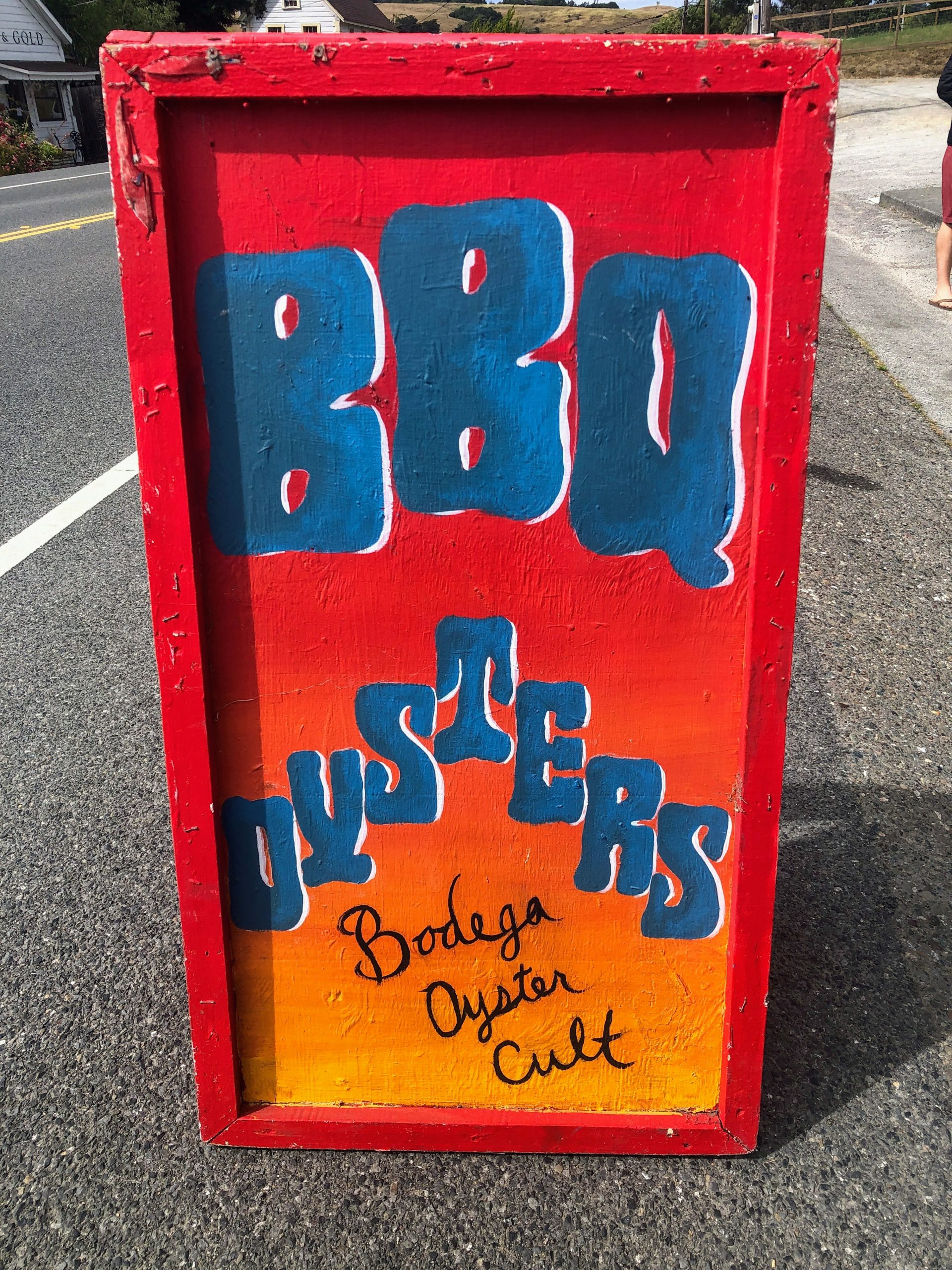 A bright red and orange sign reads BBQ Oysters Bodega Oyster Cult on blue and black letters.